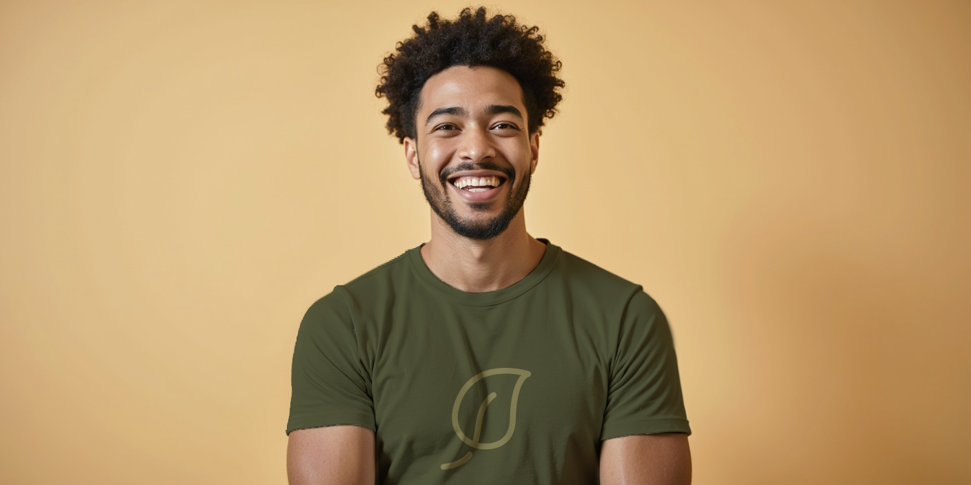 A man stands against a light tan background, wearing an olive green t-shirt featuring a subtle leaf logo on the front.