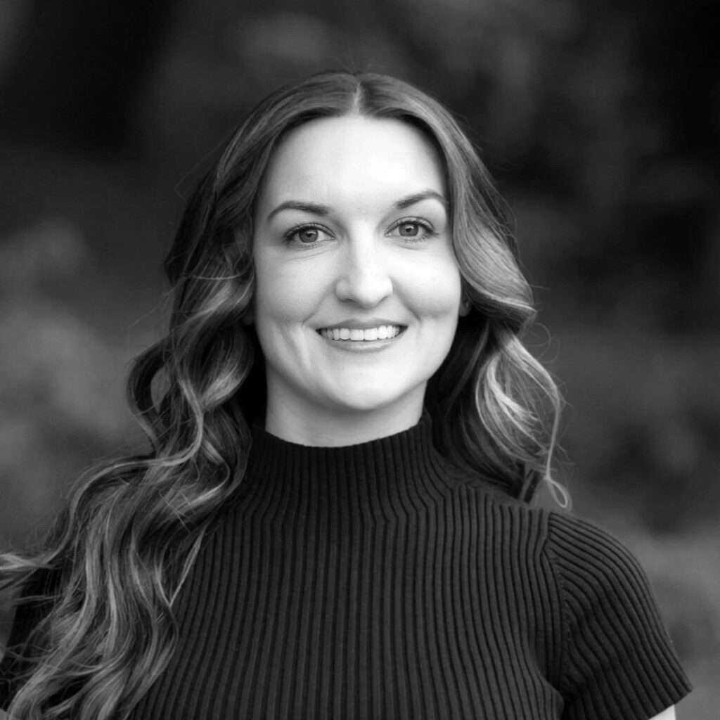Dr. Angela Weber, ND (Naturopathic Doctor), smiling outdoors in front of trees, wearing a dark short-sleeve ribbed mock-neck top.