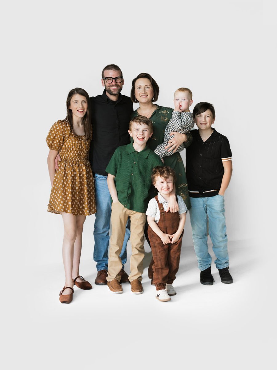 O’Brien Family The O’Brien family poses together in a studio setting with a white background. The group includes two adults (Tim and Becki O'Brien) and five children of various ages, all smiling and dressed in coordinated, casual outfits with earthy tones.